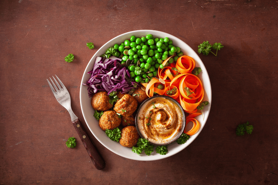 une assiettes de légumes fraichement cueillis dans un jardin permacole : petit pois, choux rouge, carotte, pomme de terre, houmous